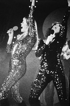 two women in sequin jumpsuits on stage with one holding her arms up