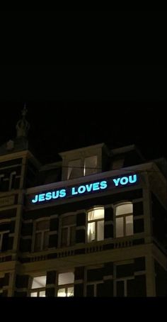 a tall building with a neon sign that says jesus loves you