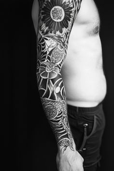 A person with a detailed, full-sleeve blackwork tattoo on their arm, standing against a dark background. Best Sleeve Tattoos Men, Geometric Tattoo Sleeve