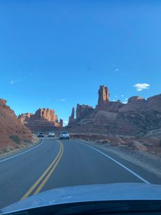 two cars driving down the road in front of some red rocks and rock formations on either side