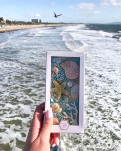 a person holding up an altered photograph in front of the ocean with seashells and starfish