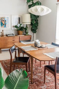 a dining room table and chairs in front of a window with potted plants on it