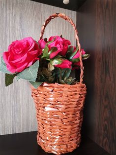 a basket filled with pink roses on top of a wooden table next to a wall