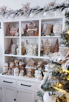 a white christmas tree with lots of small houses on it's shelves and decorations