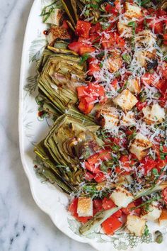 a white plate topped with artichokes covered in parmesan cheese and tomatoes