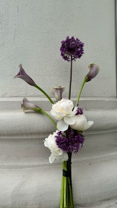 a vase filled with purple and white flowers on top of a stone pillar next to a wall