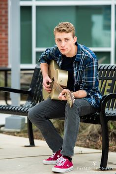 a young man sitting on a bench playing an acoustic guitar