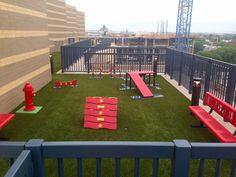 an outdoor play area with red benches and fire hydrant on the grass in front of a building