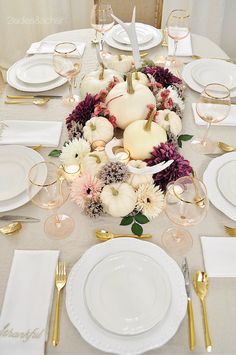 the table is set with white and gold plates, silverware, and pumpkins