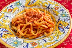 a plate full of spaghetti with sauce on it and a red table cloth behind it