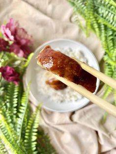 two chopsticks with food on them sitting next to some flowers and plants in the background