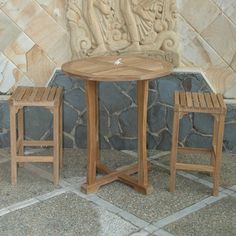 two wooden chairs and a table in front of a stone wall with carvings on it