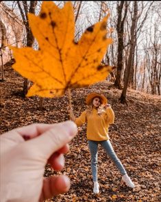 a woman holding up a yellow leaf in the woods