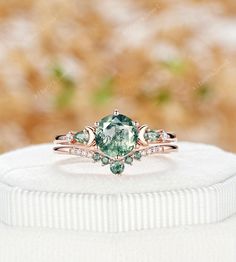 a ring with an oval cut green stone and two diamonds on the band, sitting on top of a white sweater