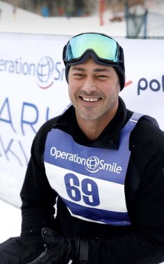 a smiling man with ski goggles on sitting in the snow