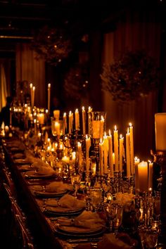 a long table with many lit candles and plates on it, all set up for a formal dinner