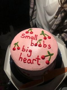 a pink cake with writing on it sitting in a white box next to a woman