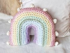 a crocheted rainbow pillow sitting on top of a bed next to a white pillow