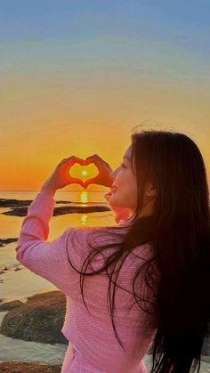 a woman standing on top of a beach holding a heart shaped object in front of her face