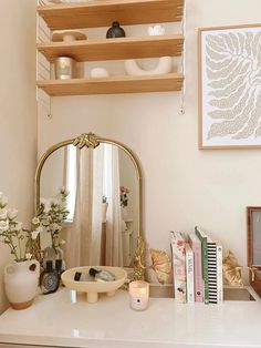 a white dresser topped with a mirror next to a shelf filled with books and vases