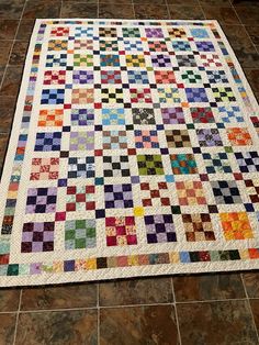 a multicolored quilt on the floor in a room with tile floors and walls