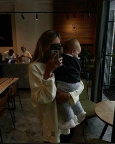 a woman holding a baby taking a selfie with her cell phone at an outdoor restaurant