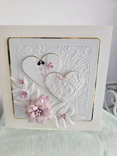 a white card with two hearts and pink flowers on the front, sitting on top of a table