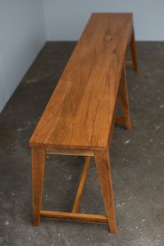 a wooden bench sitting on top of a cement floor next to a white wall in a room