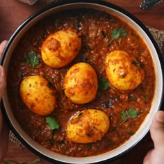 two hands holding a bowl of food with three eggs in it and garnished with parsley