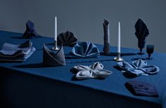 an arrangement of folded napkins and candle holders on a blue table cloth covered table