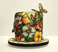 a stained glass top hat with flowers and a dragonfly sitting on it's side