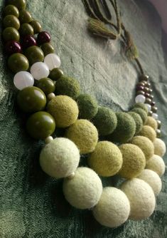 several different beads are hanging on a green cloth covered wall, and one beaded necklace is attached to the fabric