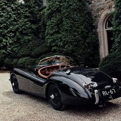 an old black sports car parked in front of a large building with ivy covered walls