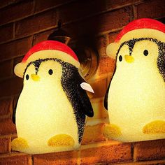 two penguins wearing hats are hanging from a brick wall