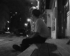 black and white photograph of two boys sitting on a bench at night in the city