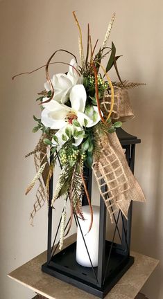 a vase with white flowers and greenery in it on a table next to a wall