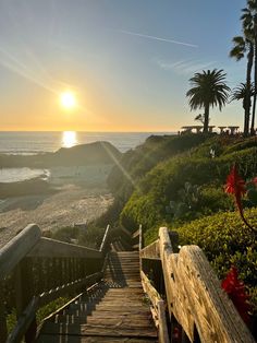 stairs lead down to the beach as the sun sets over the ocean in the background