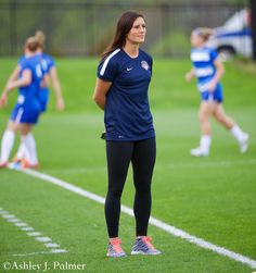 a female soccer player is standing on the field with her team mates in the background