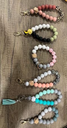 four bracelets with different colored beads and tassels hanging from them on a wooden surface