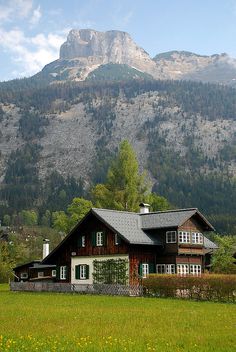 a large house in the middle of a field with mountains in the backgroud