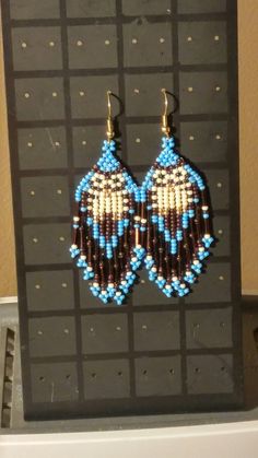 a pair of beaded earrings hanging from a hook in front of a black board