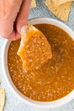 a hand dipping tortilla chips into a bowl of salsa