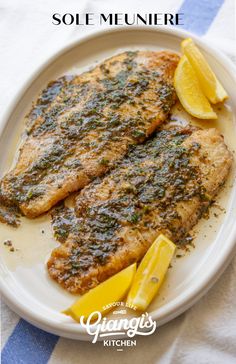 two fish fillets on a plate with lemon wedges