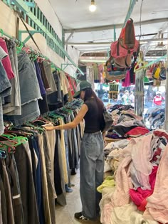 a woman standing in front of a rack of clothes at a clothing store with lots of shirts hanging on the racks