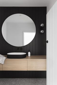 a bathroom with a round mirror on the wall next to a wooden counter and sink