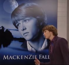 a man standing in front of a large poster with the name mackenzie fall on it