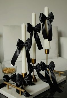 four candles with black bows on them sitting on a white tray in front of a couch