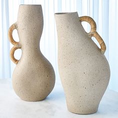 two white vases sitting on top of a table next to each other with handles