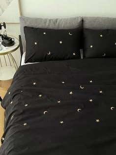 a black comforter with gold stars and moon designs on it, next to a night stand