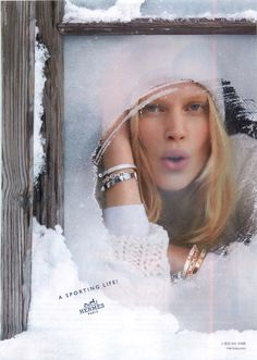 a woman with her hand on her head in front of a window covered in snow